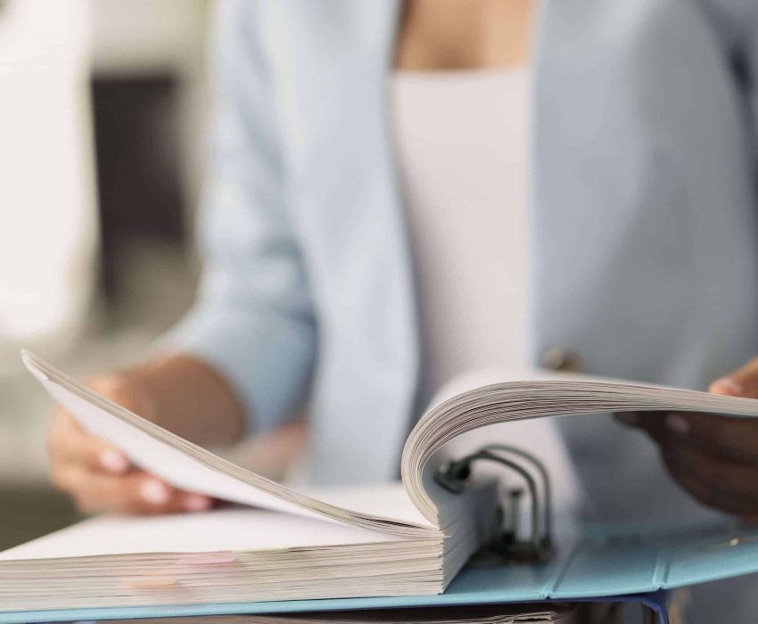 Person blättert durch Dokumente im Ordner
