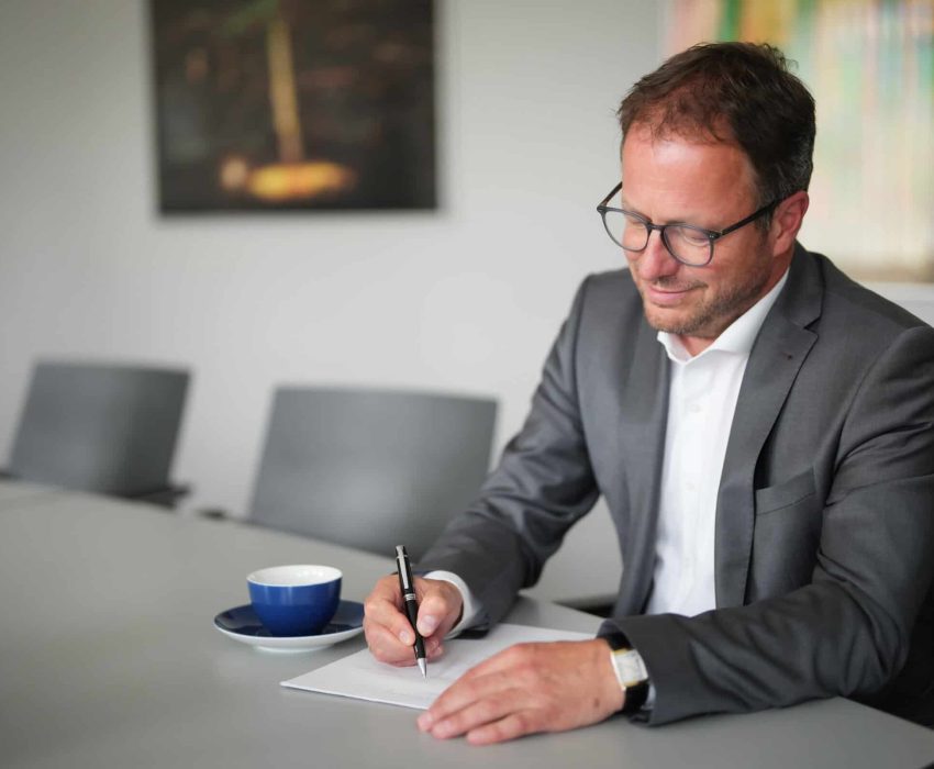 Klaus Schüttler im Anzug schreibt an einem Tisch