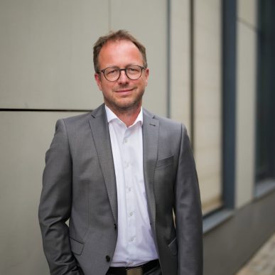 Klaus Schüttler im Anzug vor moderner Gebäudewand